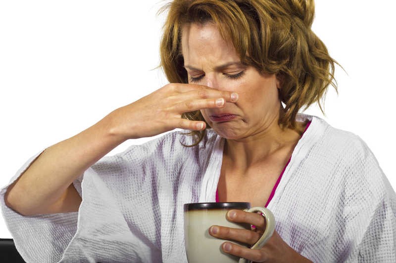photo of a female in bath robe holding a mug in one hand and the other hand pinching her nose.