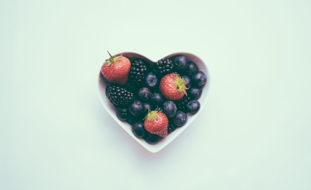 Photo of a heart shaped bowl with strawberries, black berries and blueberries.