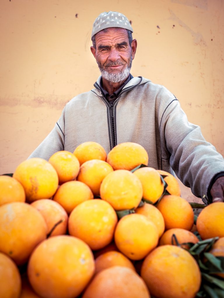 Photo of man behind a mound of oranges.