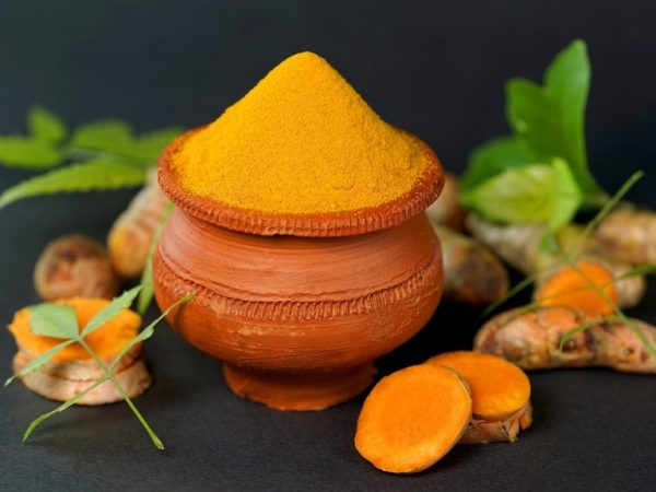 Photo of turmeric powder and turmeric root in clay dish